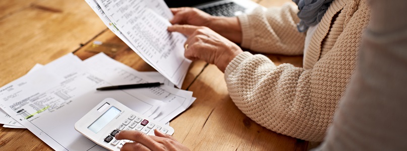 two people looking at their bills using a calculator and a laptop